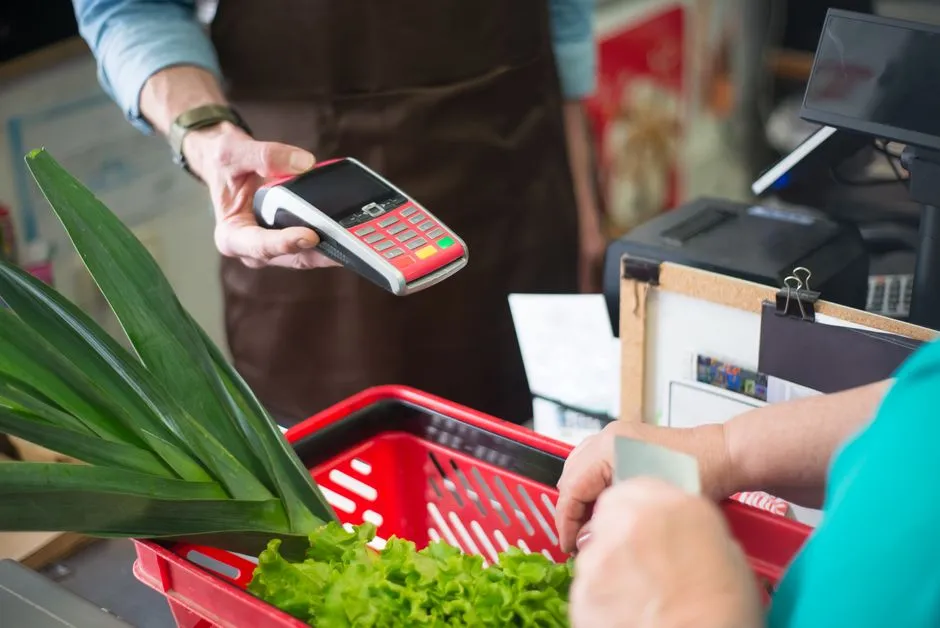 A shopper paying at a grocery store checkout counter with fresh produce in the basket